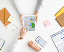 View of hands of two contemporary analysts or brokers discussing financial data on touchscreen while one of them pointing at circle diagram